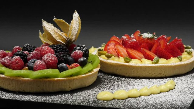 Crostata ai frutti di bosco con crema, fragole, lamponi, ribes, more, kiwi.
Piatto di lavagna nera con torte ai frutti di bosco e zucchero a velo. Pasticceria professionale.