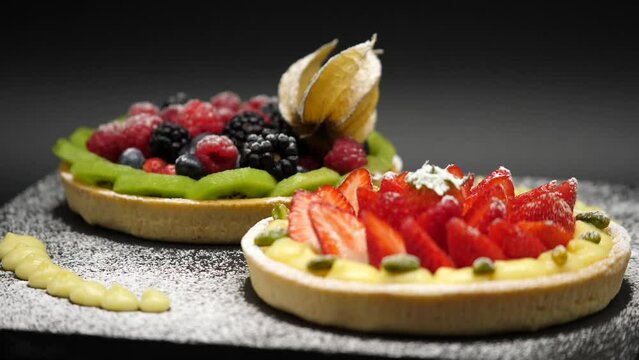 Crostata ai frutti di bosco con crema, fragole, lamponi, ribes, more, kiwi.
Piatto di lavagna nera con torte ai frutti di bosco e zucchero a velo. Pasticceria professionale.