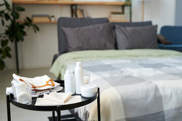 Group of bodycare items for baby on small round table against double bed with cushions and duvet in spacious bedroom
