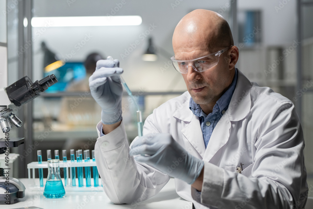 Aufkleber mature experienced scientist in protective workwear mixing two chemical substances in flask while si