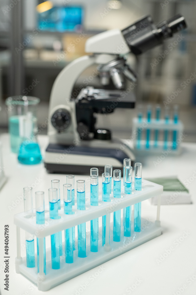 Poster group of flasks with samples of blue liquid standing on workplace of scientist against microscope an