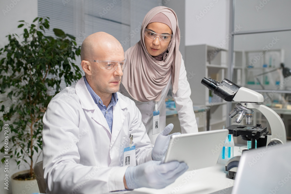 Aufkleber two young contemporary virologists discussing online data in laboratory whilemature male scientist p