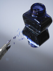 Vertical selective focus shot of a pen, an ink bottle on a mirror table and blue ink spilled on it