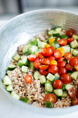 Farro in silver bowl with chopped cucumbers and tomatoes