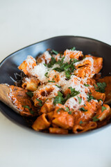 pasta with a vodka sauce, parmesan and parsley in a black ceramic bowl with wooden serving utensils