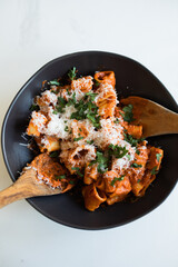 pasta with a vodka sauce, parmesan and parsley in a black ceramic bowl with wooden serving utensils