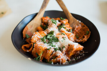 Rigatoni with a vodka sauce, parmesan and parsley in a black ceramic bowl with wooden serving utensils