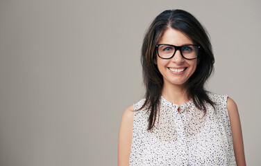 Spectacled beauty. Portrait of an attractive young woman smiling against a gray background.