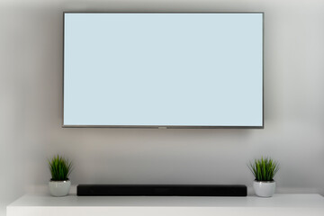 Blank white smart TV screen in grey, bright mockup, front view. Empty telly LED display in living room mock up. Clear panel monitor including sound bar and artificial grass in the pot. 