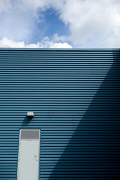 Vertical Shot Of The Facade Of A Dark Blue Building With White Door And Lighting Bulb On It