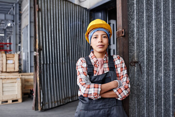 Young confident Hispanic female engineer in coveralls and protective helmet crossing arms by chest...