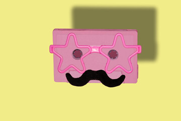 
pink cassette with pink star glasses and mustache, creative fashion art design music retro cassette on a yellow background