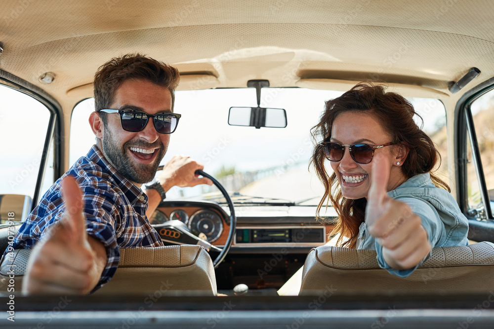 Poster thumbs up for roadtrips. rearview portrait of an affectionate couple giving you a thumbs up while en