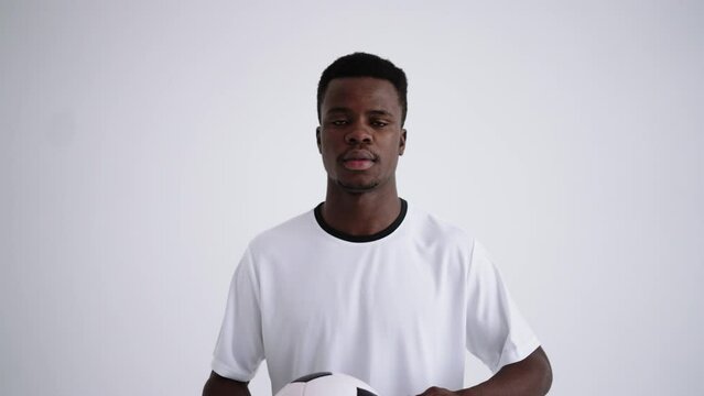 portrait of serious junior sportsman in football uniform with ball in hands in white studio
