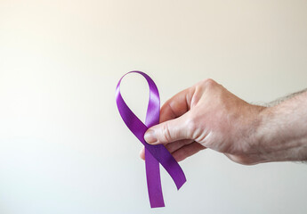 A male hand is holding a purple ribbon.