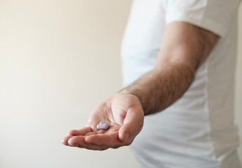 A male hand is holding a purple pill.