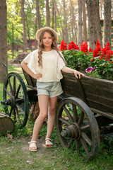 Tween girl standing near flowerbed shaped as wooden cart with blooming red salvia in park
