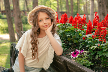 Dreamy cute tween girl sitting near flower bed with red salvia in summer park