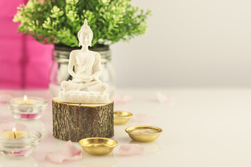 Buddha statue on a wooden podium, rose petals and candles on a white table