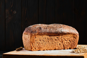 Homemade crusty whole grain bread on a wooden background. Dark mood. Traditional techniques loaf, innovating bread, slow carb baking