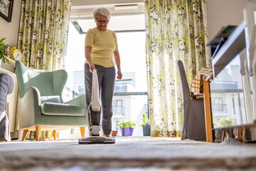 Senior woman using vacuum cleaner to clean the house
