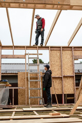 Two construction company workers assemble a wooden frame house. One builder is standing on the roof