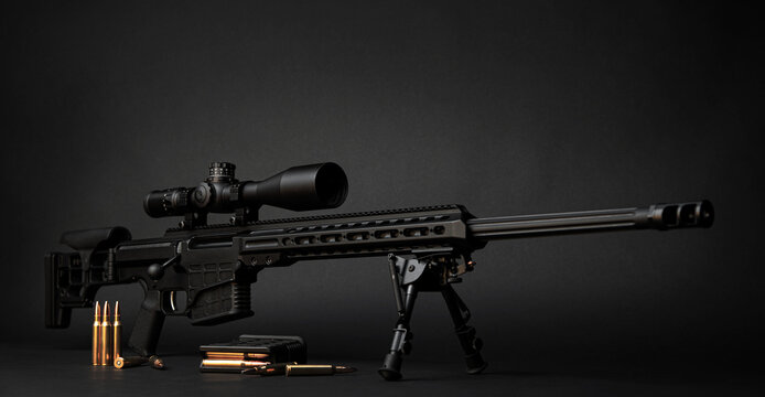 Modern powerful sniper rifle with a telescopic sight mounted on a bipod. Ammo and an additional magazine next to the rifle.