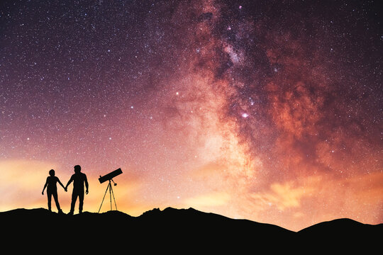 Silhouettes of people in the night. A couple in love is stands on the hill and looks at the bright milky way galaxy.