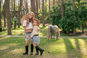 Happy preteen girls embracing in green park with pony eating grass behind