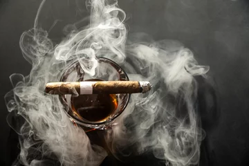 Foto op Plexiglas Whiskey drinks with cigars from Cuba Havana on black background. A glass of whiskey or cognac with a Smoking cigar lying on top. Top down view. © Василь Івасюк