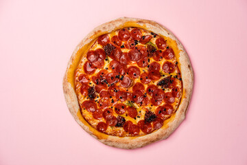 Pizza with Chorizo sausage, sweet pepper, sun-dried tomatoes, dried chilli, gouda cheese and mozzarella cheese with pilati sauce, thin crust and lush board. Pink background. Copy space. Top view