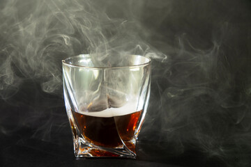 Whiskey drinks isolated on black backdrop. Close up view of a glass of whiskey on a black slate with a smoky background.