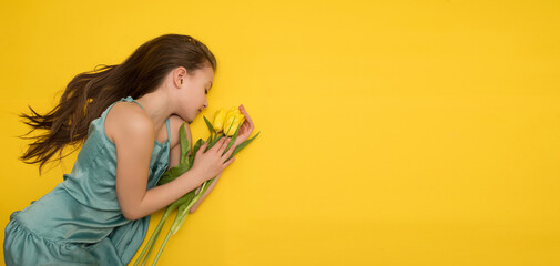 a little girl with long dark hair with a bouquet of yellow tulips on a yellow background, a place for text