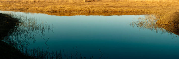 blue calm pond in springtime sunny weather. Dry yellow grass on shores. Nice place to try catch your first fish
