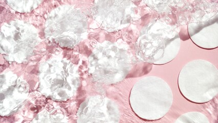 Cotton pads arranged in rows on pink background with water ripples over them | Background for...