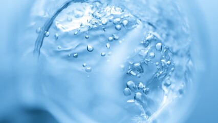 Top view macro shot of transparent liquid pouring into beaker creates a lot of bursting bubbles on blue background | Abstract face care cosmetics formulation concept