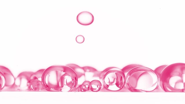 Macro shot of pink clear different sized bubbles are falling down on white background | Abstract skin care cosmetics with retinol formulation concept