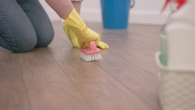 a housewife in yellow gloves is trying to clean the parquet floor with a brush.