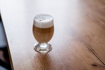Caffe latte macchiato coffee layered with milk in a high drinking glass on a wooden table. 