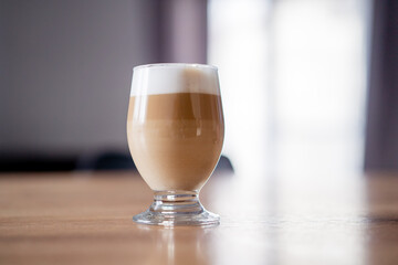 Caffe latte macchiato coffee layered with milk in a high drinking glass on a wooden table. 