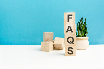 FAQS - word is written on wooden cubes on a blue background. close-up of wooden elements. In the background is a green flower. - obrazy, fototapety, plakaty