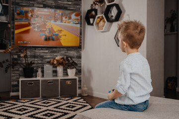Fototapeta na wymiar Happy boy playing video games holding game controller sitting on the coach in living room