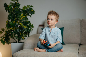 Happy boy playing video games holding game controller sitting on the coach in living room