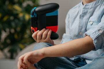 Happy boy playing video games holding game controller sitting on the coach in living room