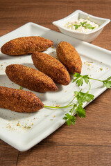 Vegan food, vegan kibbeh and sauce on a white plate, over wood, selective focus.