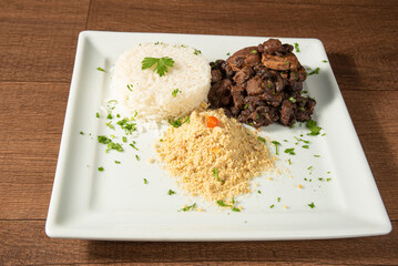 Vegan food, vegan feijoada, rice and farofa on a white plate, over wood, selective focus.