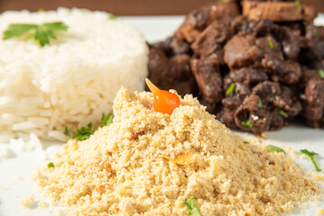 Vegan food, vegan feijoada, rice and farofa on a white plate, over wood, selective focus.
