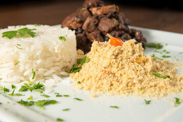 Vegan food, vegan feijoada, rice and farofa on a white plate, over wood, selective focus.