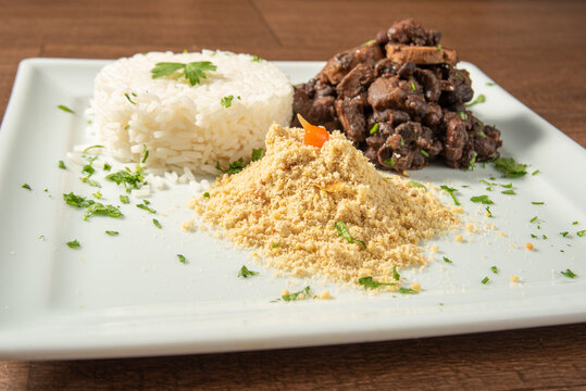 Vegan food, vegan feijoada, rice and farofa on a white plate, over wood, selective focus.
