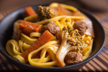 Vegan food, Vegan Yakisoba, with chopsticks in a bowl on bamboo mat, over wood, selective focus.